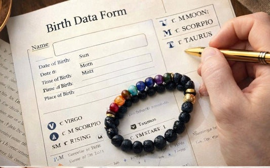 Hand holding a pen over a birth data form with a chakra bracelet on top